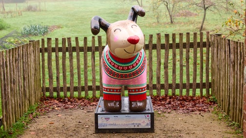 A sculpture of a Snowdog, with a red nose and a painted-on Christmas jumper, standing in the archway entrance to the Walled Garden.